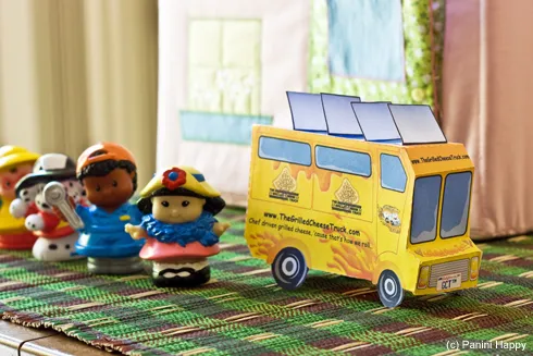 Ein kleines Papiermodell des Grilled Cheese Trucks mit Spielzeugfiguren, symbolisiert Freude für kleine Feinschmecker