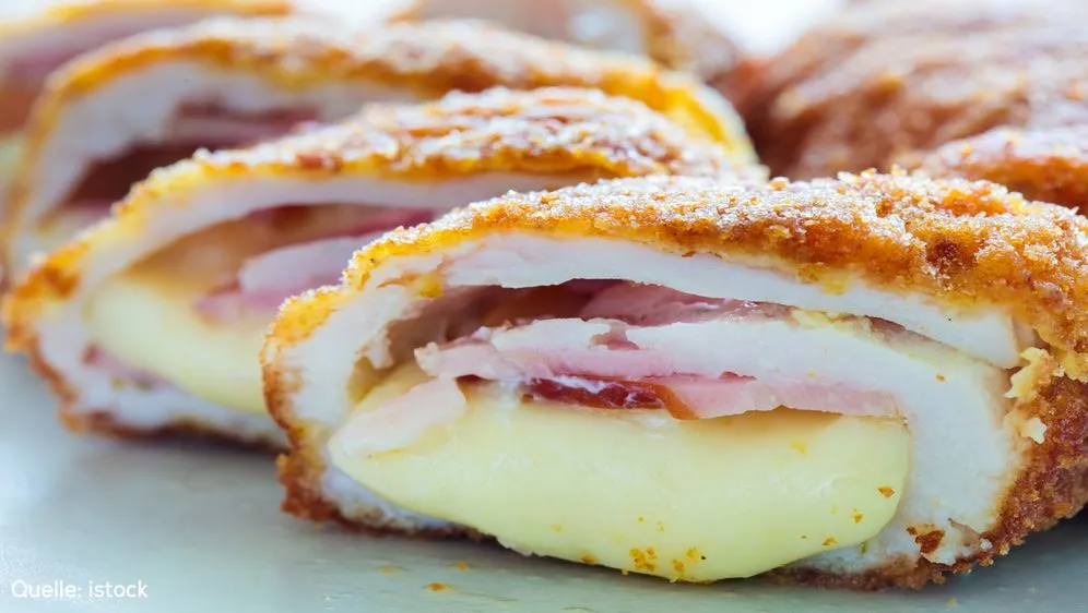 Ein knuspriges Cordon Bleu mit geschmolzenem Käse und Schinken, umgeben von frischen Zutaten, die zur Individualisierung angeboten werden, symbolisiert den beliebten "Cordon Bleu Tag".