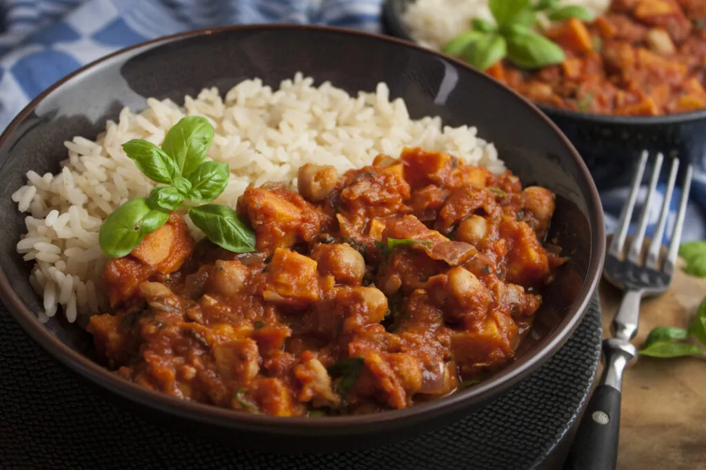 Ein köstlicher vegetarischer Süßkartoffel-Kichererbsen-Schmortopf, garniert mit frischem Basilikum und bereit zum Genießen.