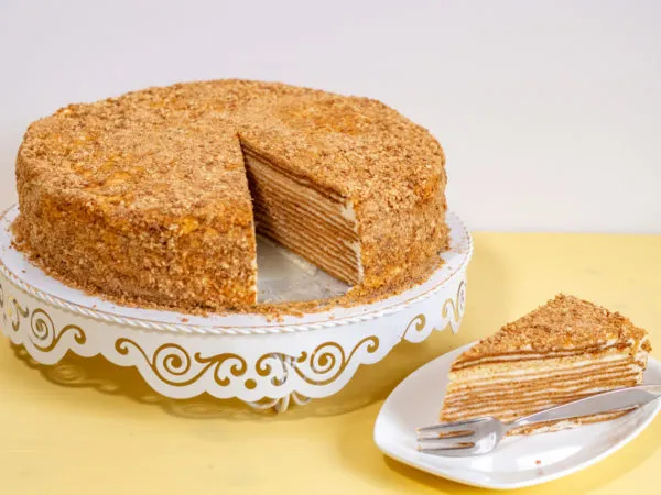 Ein kunstvoll geschichteter russischer Honigkuchen (Medovik), von oben fotografiert, mit hellbraunen Teigschichten und cremiger Füllung, bestreut mit Kuchenkrümeln.