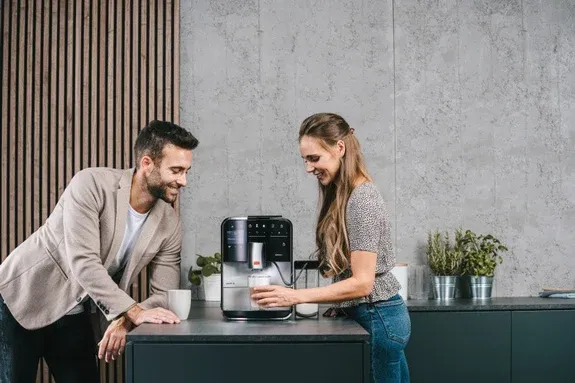 Ein lächelndes Paar bereitet Kaffee mit einem Kaffeevollautomat mit Milchsystem in einer modernen deutschen Küche zu.