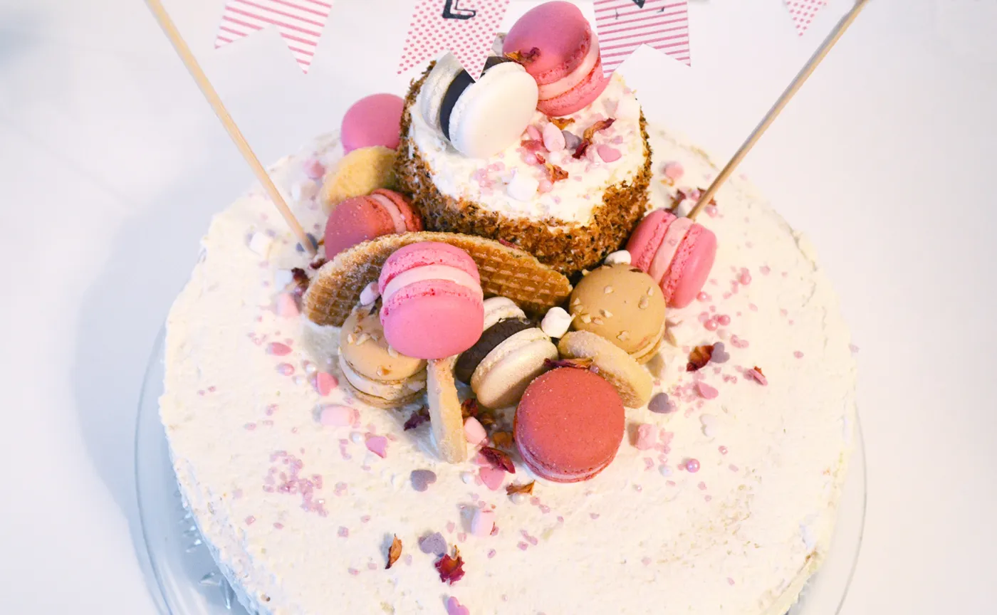 Ein liebevoll dekorierter, rosa Geburtstagskuchen mit Kokos-Ananas-Füllung und festlichen Fähnchen, perfekt für einen tollen Geburtstagskuchen.