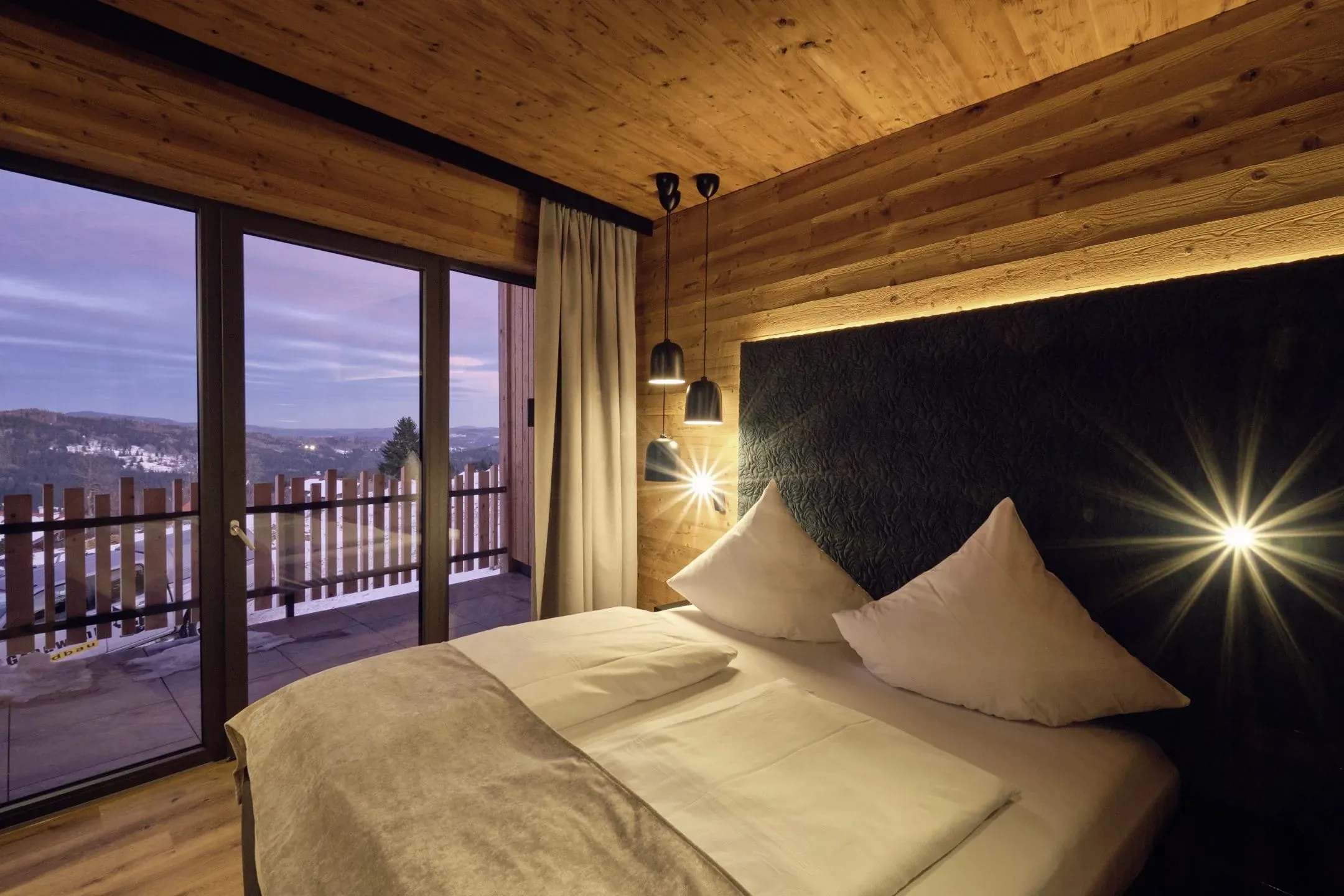 Ein luxuriöser Schlafbereich in einem Loft des Hunderesort Waldeck mit bodentiefen Fenstern, Balkon und Panoramablick über den Bayerischen Wald – ideal für einen stilvollen Urlaub mit Hund.