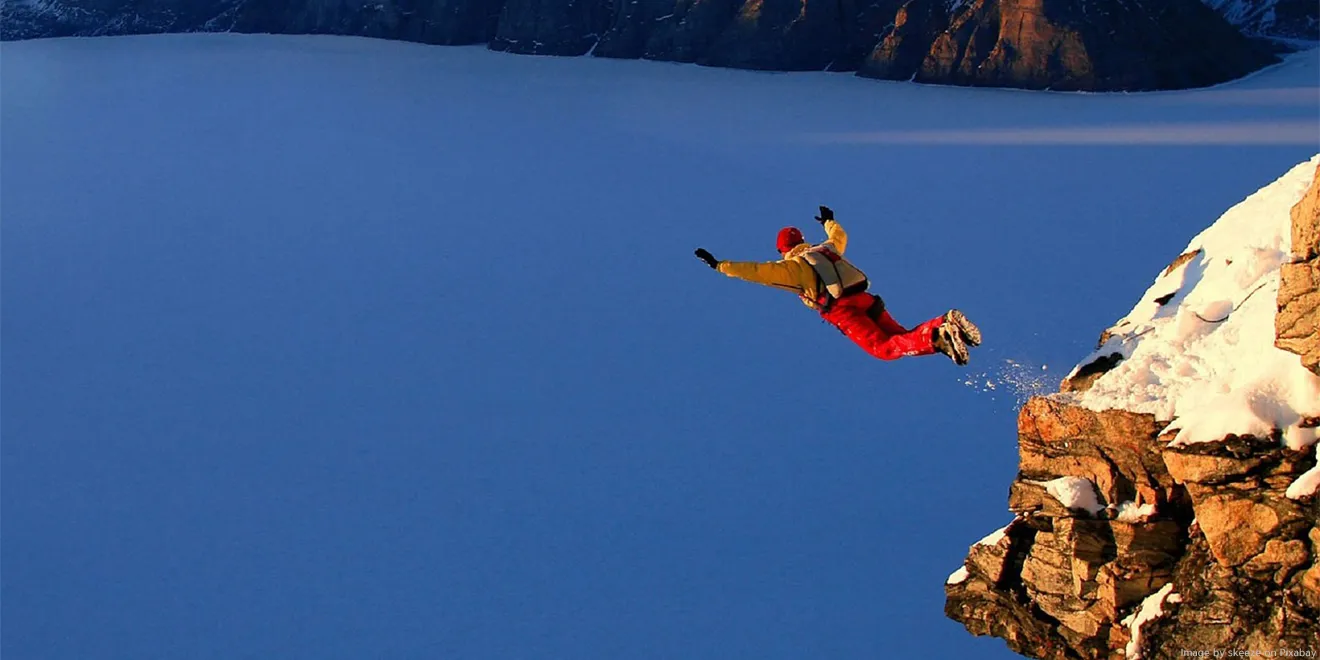 Ein Mann springt mit einem Fallschirm von einem Felsen