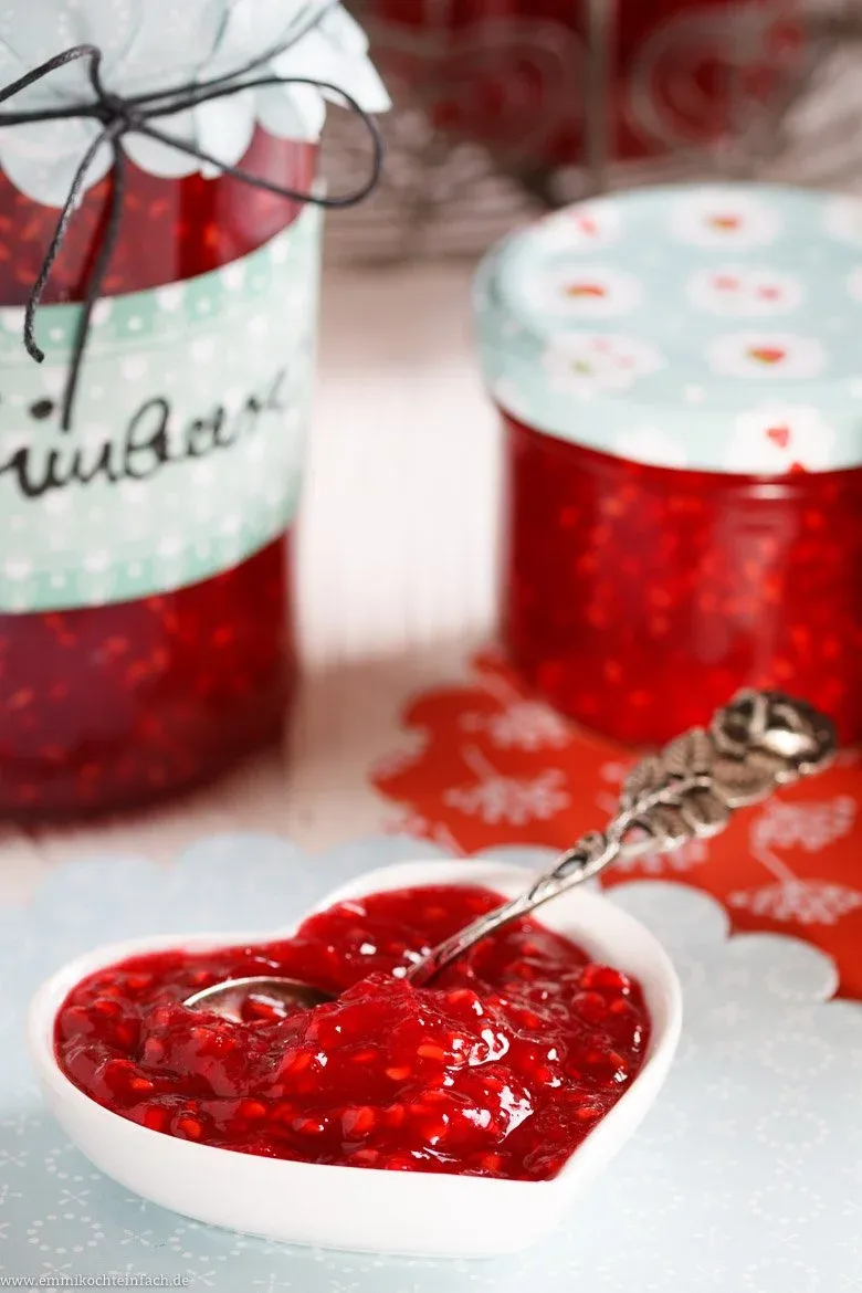 Ein Marmeladenglas voll leuchtend roter Himbeermarmelade, das das Ergebnis einer einfachen und beliebten deutschen Einkochmethode zeigt.