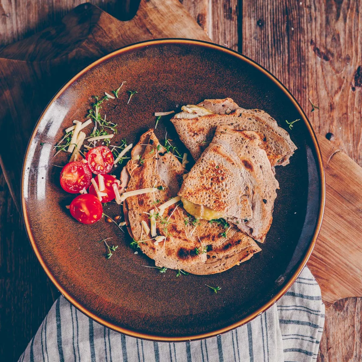 Ein mit veganer Sour Cream bestrichener Buchweizenpfannkuchen, der mit veganem Käse bestreut und wie eine Quesadilla gebacken wird, bis der Käse geschmolzen ist.