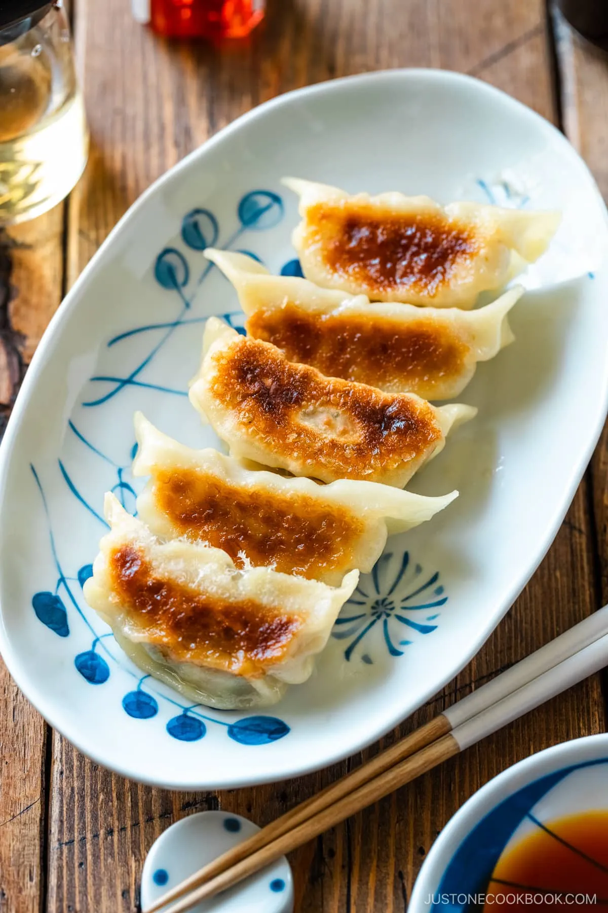 Ein ovaler Teller mit Gyoza (japanische Teigtaschen oder gebratene Klöße) mit einer kleinen Schale Dip-Sauce aus Sojasauce, Essig und japanischem Chiliöl.