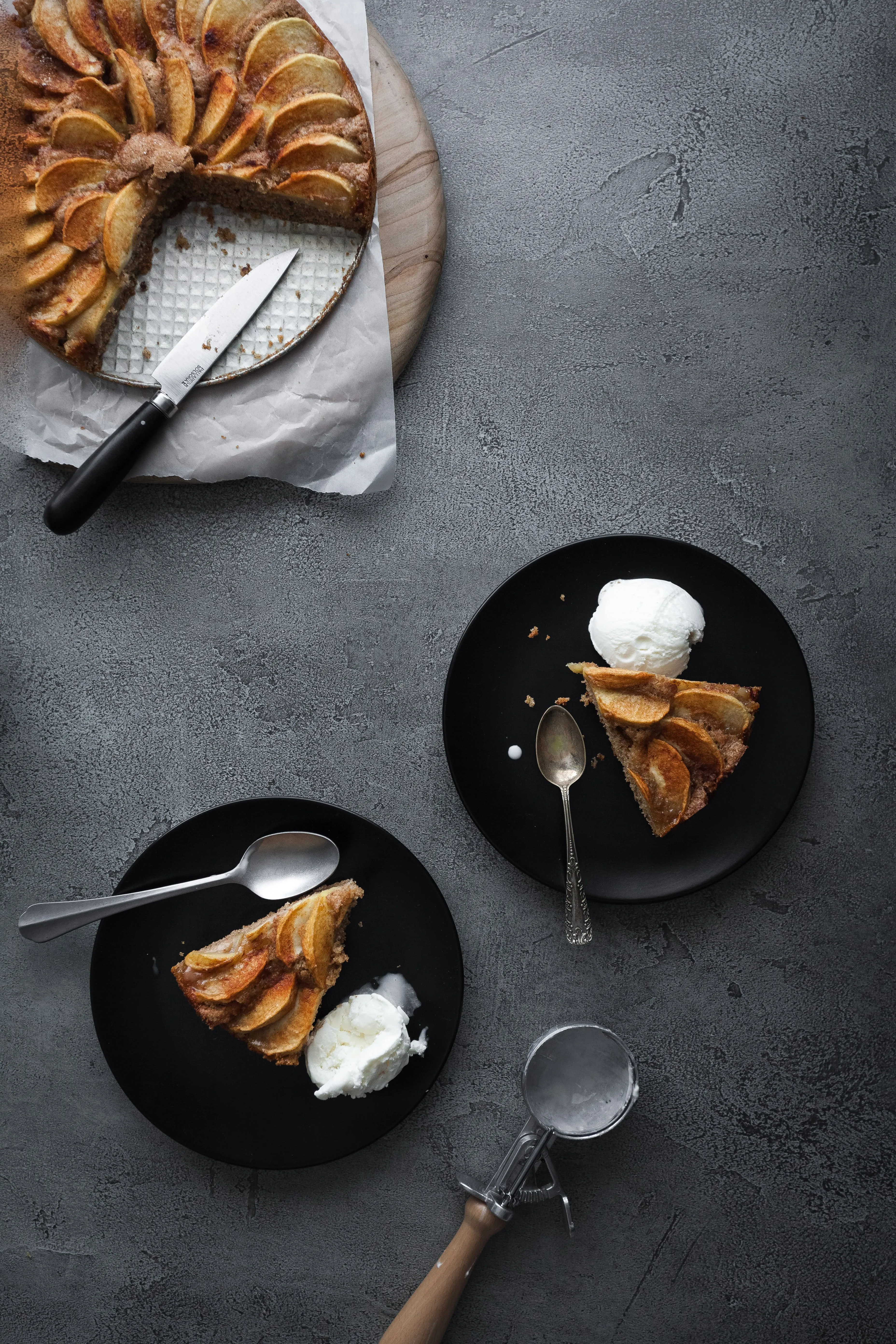 Ein overhead-Bild eines veganen deutschen Apfelkuchens mit zwei Stücken auf Tellern, dazu Eiscreme.