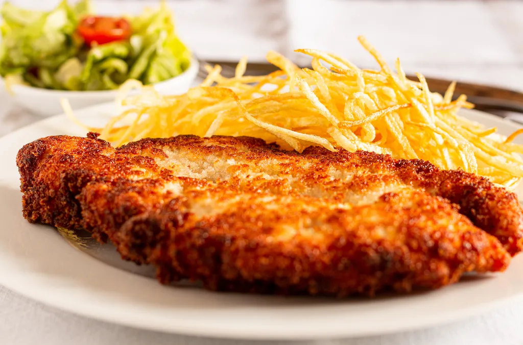 Ein perfekt gebratenes, goldbraunes Hähnchenschnitzel, knusprig paniert und appetitlich angerichtet, bereit zum Servieren mit frischer Zitrone.