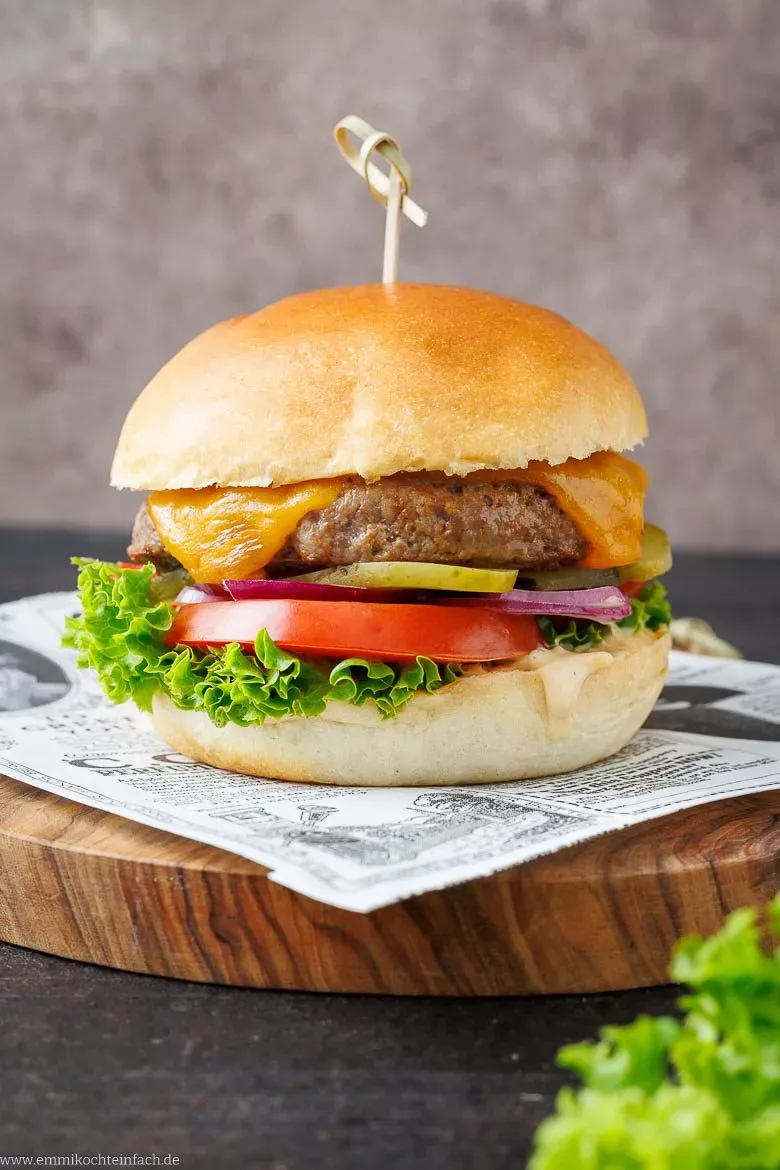 Ein perfekt zubereiteter Hamburger mit saftigem Rindfleischpatty, frischem Salat, Tomate, Zwiebel und schmelzendem Käse, angerichtet auf einem rustikalen Holzbrett.
