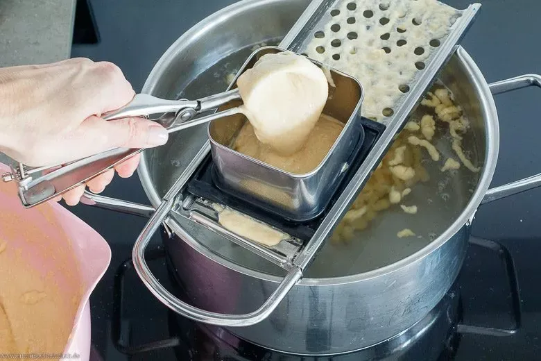 Ein praktischer Spätzlehobel aus Edelstahl liegt auf einem Kochtopf, bereit um Knöpfle oder kurze Spätzle direkt ins Wasser zu hobeln.