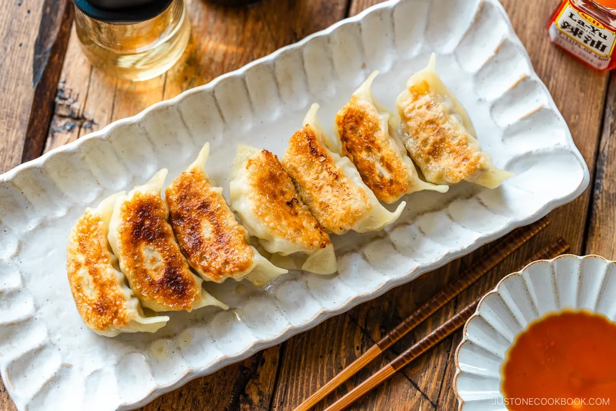 Ein rechteckiger Teller mit Gyoza (japanische Teigtaschen oder gebratene Klöße) mit einer kleinen Schale Dip-Sauce aus Sojasauce, Essig und japanischem Chiliöl.