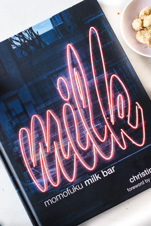 Ein reich verziertes Backbuch mit dem Titel &quot;Milk Bar&quot; liegt offen neben einer Tasse Kaffee, was die Liebe zum Backen unterstreicht