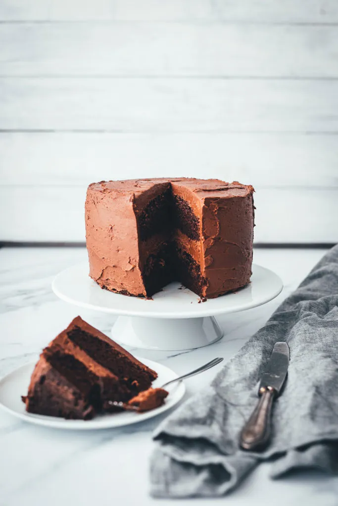 Ein reichhaltiger Geburtstagskuchen mit Schokolade, der sorgfältig mit einer dicken Schicht Schoko-Frosting bedeckt ist, bereit zum Anschneiden.