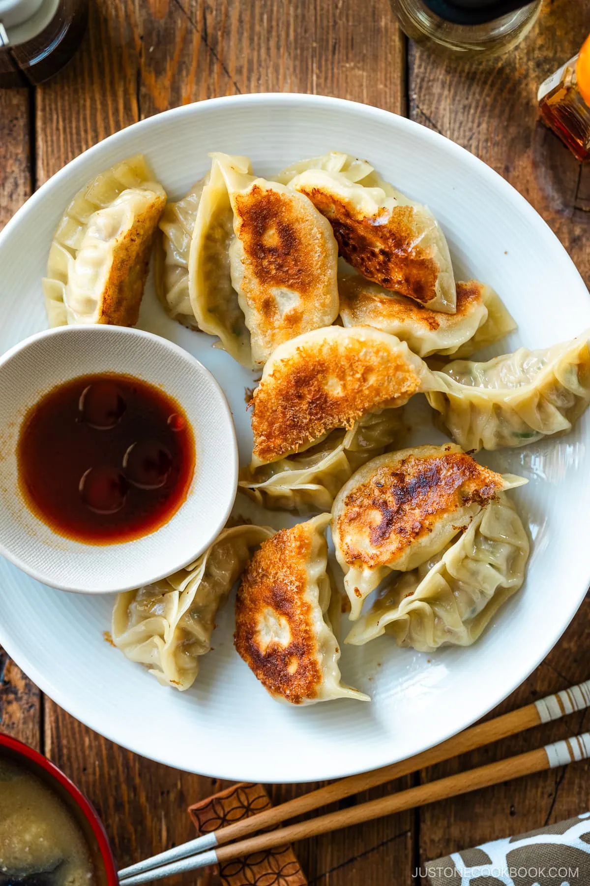 Ein runder Teller mit Gyoza (japanischen Teigtaschen oder gebratenen Klößen) mit einer kleinen Schale Dip-Sauce aus Sojasauce, Essig und japanischem Chiliöl.