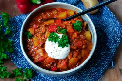 Ein rustikaler Bauerntopf mit Hackfleisch, Kartoffeln und Paprika in einer Keramikschüssel, garniert mit frischer Petersilie.
