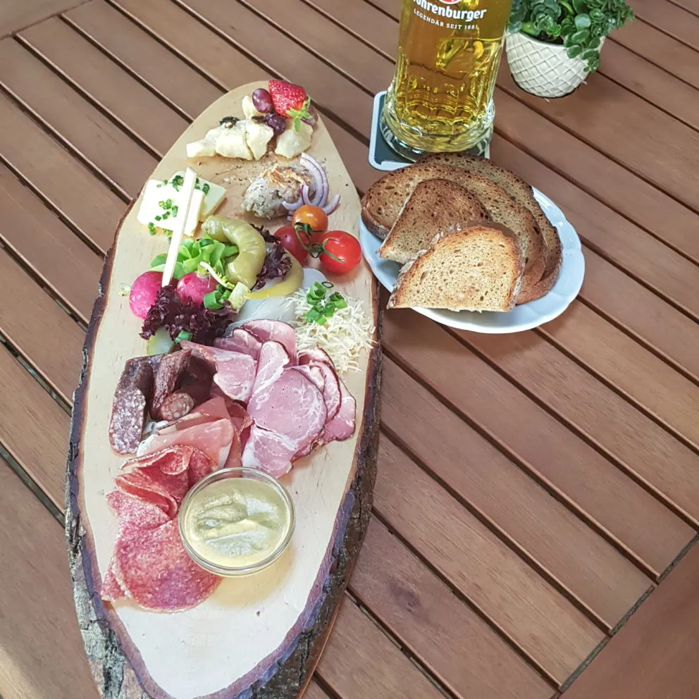 Ein rustikales Brotzeitbrett mit verschiedenen Wurst- und Käsesorten, garniert mit frischem Gemüse und Brot, präsentiert in einem traditionellen deutschen Gasthaus.