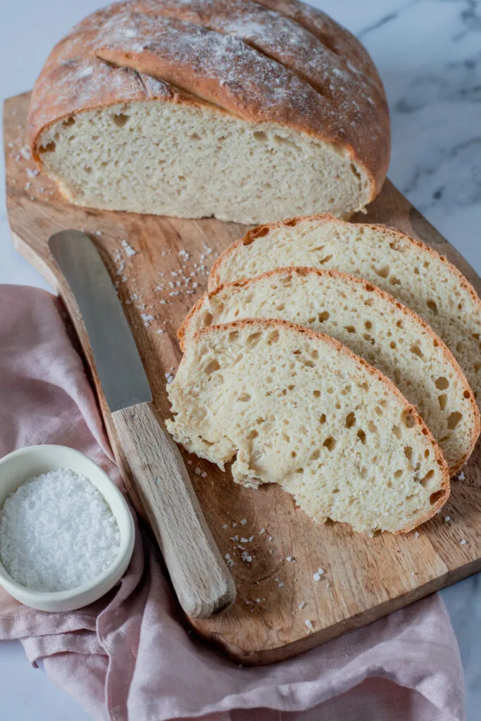Ein rustikales, goldbraunes Brot liegt auf einermeti einer Holzunterlage, bereit zum Anschneiden.