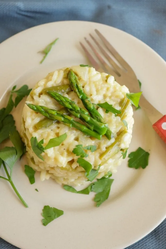 Ein Schälchen mit veganem Spargelrisotto, dekoriert mit Hefeflocken, die für einen käsigen Geschmack sorgen. Der Fokus liegt auf der Textur des Risottos und der leuchtenden Farbe des grünen Spargels.