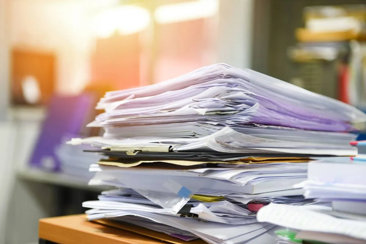 Ein Schreibtisch ist mit einem Stapel von Dokumenten und Rechnungen bedeckt, was die Notwendigkeit einer digitalen Lösung wie einem Rechnungsprogramm mit DATEV-Schnittstelle verdeutlicht.