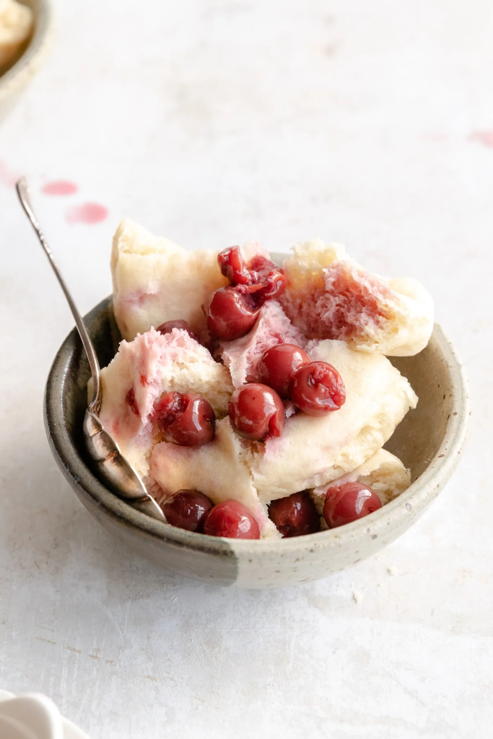 Ein Schüssel mit zerteilten Hefeklößen, übergossen mit glänzenden Sauerkirschen und Saft.