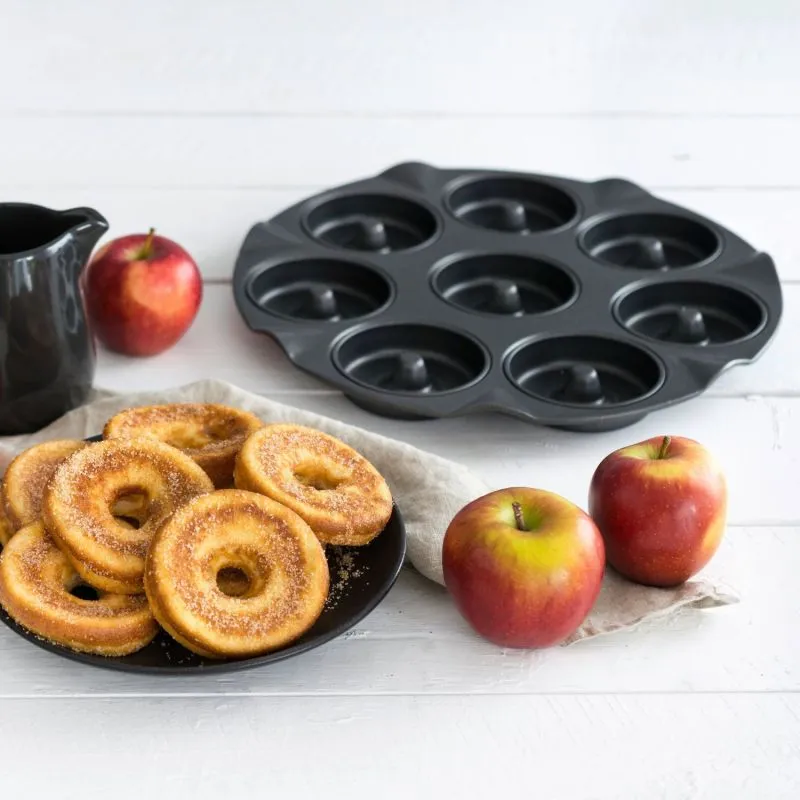 Ein spezialisiertes Backblech für Apfelküchli, umgeben von Äpfeln und fertigen gebackenen Leckereien