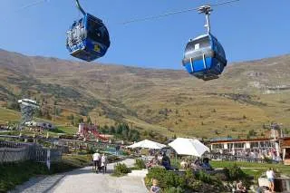 Ein Spielplatz in einer Berglandschaft, darüber schweben zwei Gondeln.