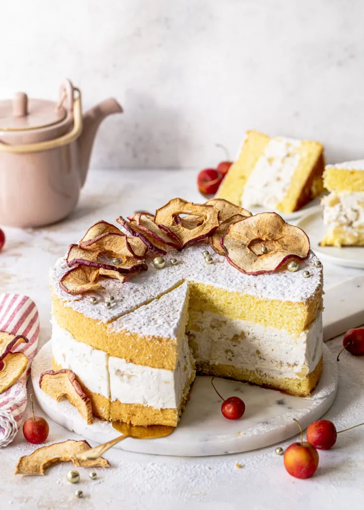 Ein Stück Bratapfel-Käse-Sahne-Torte auf einem Teller, sichtbar die Schichten aus Biskuit, Quark-Sahne-Creme und Zimtapfel-Füllung