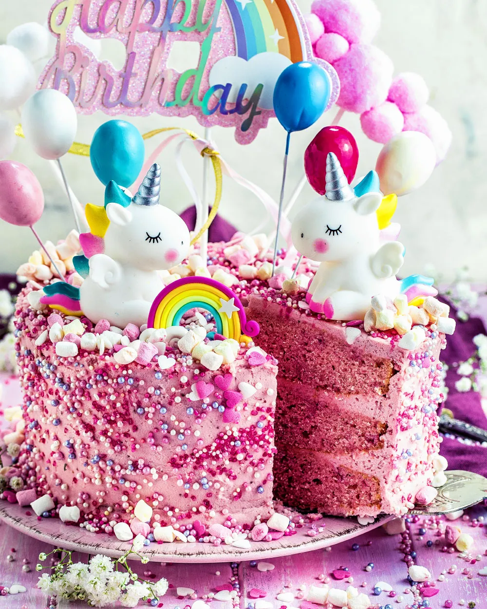 Ein Stück des Einhorn-Kuchens angeschnitten, zeigt die rosa Schichten und Mascarpone-Creme