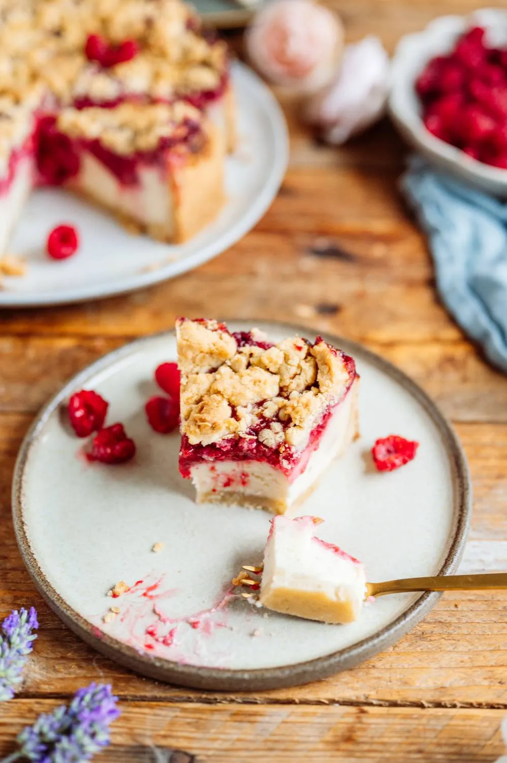Ein Stück Himbeer-Joghurt-Cheesecake wird mit einer Kuchengabel serviert, mit sichtbar cremiger Füllung und Streuseln