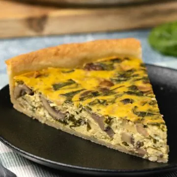 Ein Stück vegane Quiche auf einem schwarzen Teller.