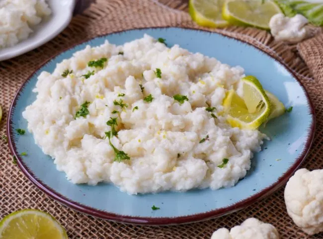 Ein Teller mit Blumenkohlpüree, garniert mit frischen Kräutern und einem Spritzer Olivenöl.