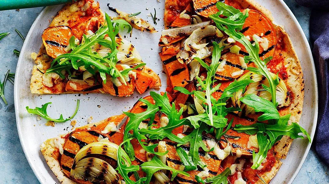 Ein Teller mit bunten Vollkorn-Wraps, gefüllt mit frischem Gemüse und Käse, die an eine vegetarische Pizza erinnern.