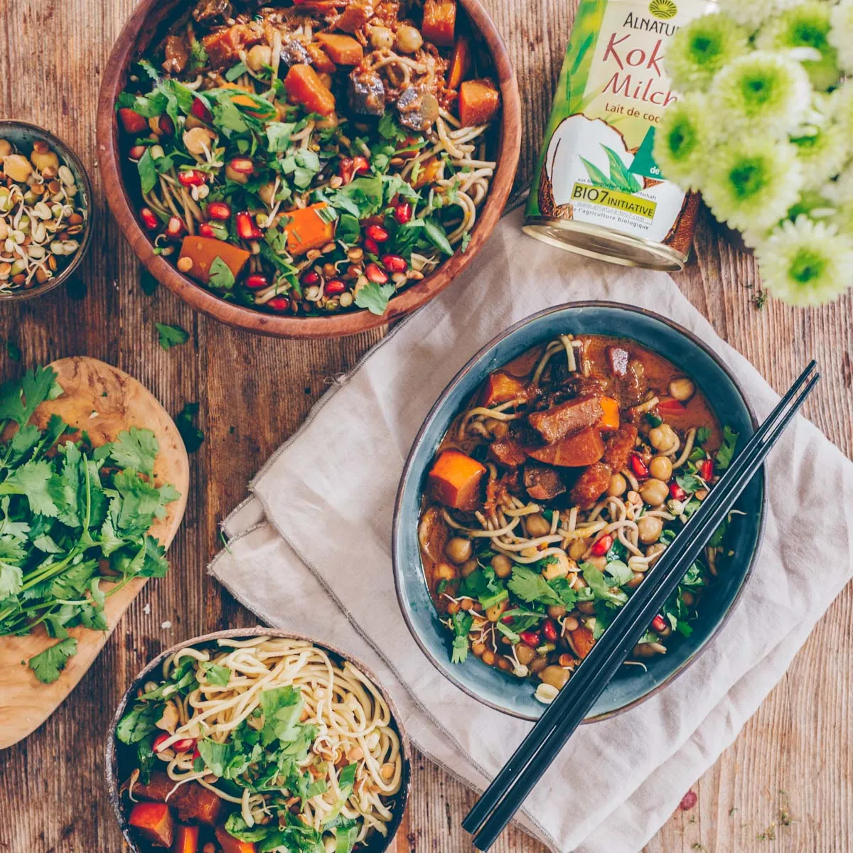 Ein Teller mit Kürbis-Curry, Mie-Nudeln, frischen Kräutern und Granatapfelkernen, der eine vollständige und appetitliche Mahlzeit darstellt.