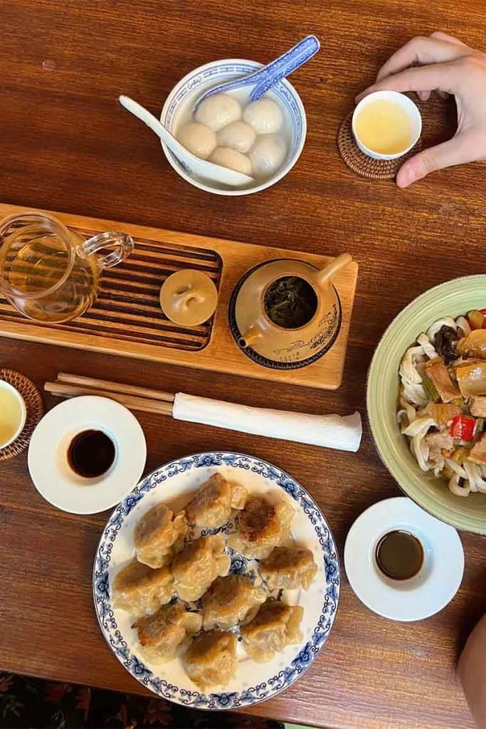 Ein Tisch im Jing Yuan Tea House in Zagreb, gedeckt mit chinesischen Spezialitäten wie Tangyuan, Teigtaschen, Udon-Nudeln und einer Teezeremonie, die ein authentisches chinesisches Erlebnis bietet.