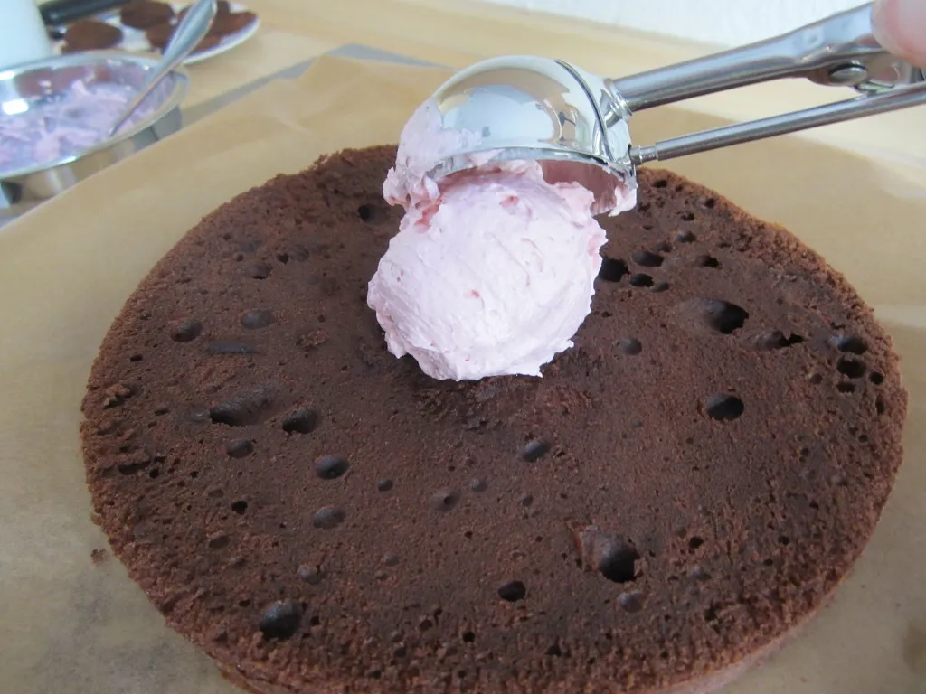 Ein Tortenboden mit einer Schicht Himbeer-Meringue-Creme, die mit einem Eislöffel aufgetragen wird