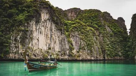Ein traditionelles Longtail-Boot ankert in einer ruhigen Bucht der thailändischen Insel Ko Phi Phi, umgeben von steilen Kalksteinfelsen.