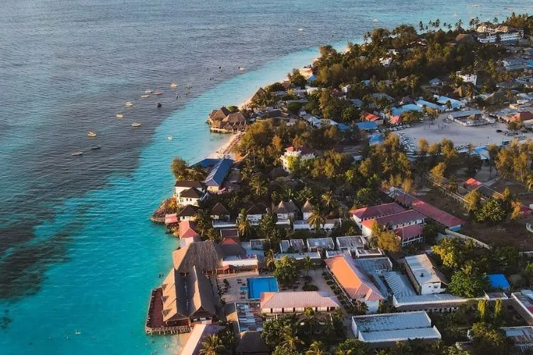 Ein typisches Dhow-Boot segelt auf dem türkisfarbenen Wasser vor einem tropischen Strand auf Sansibar