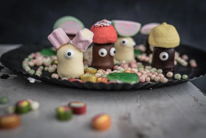 Ein von oben fotografierter, saftiger Marmorkuchen, liebevoll dekoriert mit Schokokuss-Gesichtern und bunten Süßigkeiten, perfekt für einen Kindergeburtstag.