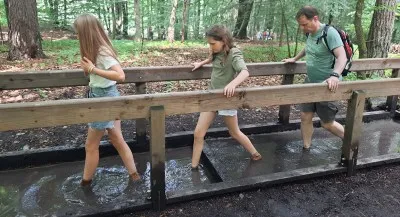Ein Weg im Barfußpark Egestorf, auf dem Menschen barfuß über verschiedene natürliche Materialien wie Holz, Steine und Sand laufen
