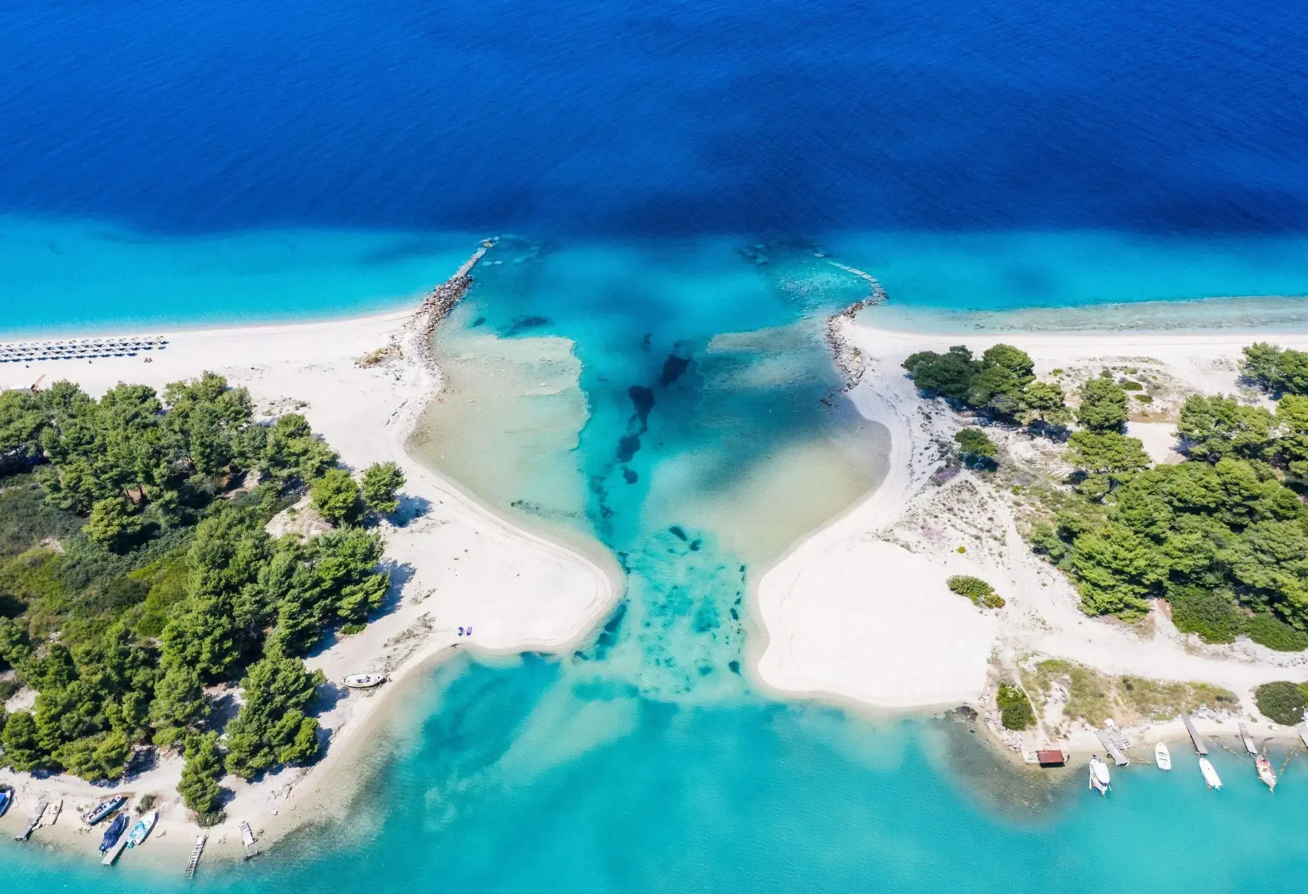 Ein weißer Sandstrand mit einer Lagune und einem Hafen mit vor Anker liegenden Booten