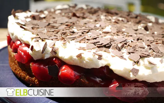 Eine appetitliche Nuss-Kirsch-Sahne-Torte auf einer Etagere, garniert mit Schokolade.