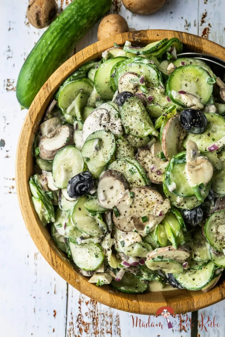 Eine Auswahl an Zutaten für einen Gurken-Champignon-Salat, darunter Gurken, Champignons, Oliven, Zwiebeln und frische Kräuter.