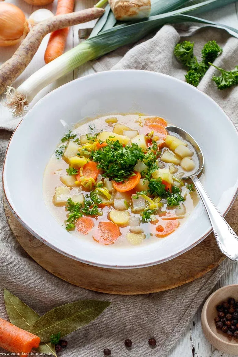 Eine dampfende Schüssel klassische Gemüsesuppe, perfekt für Anfänger, auf einem Holztisch mit frischen Kräutern.