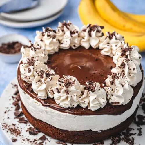 Eine einladende Schoko-Bananen-Sahne-Torte, präsentiert auf einem Tortenständer, symbolisiert traditionellen Kaffeegenuss in Deutschland.
