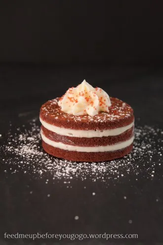 Eine einzelne Red Velvet Mini Cake, angeschnitten, um die rote Farbe des Teigs und die cremige Textur des Frostings zu zeigen.