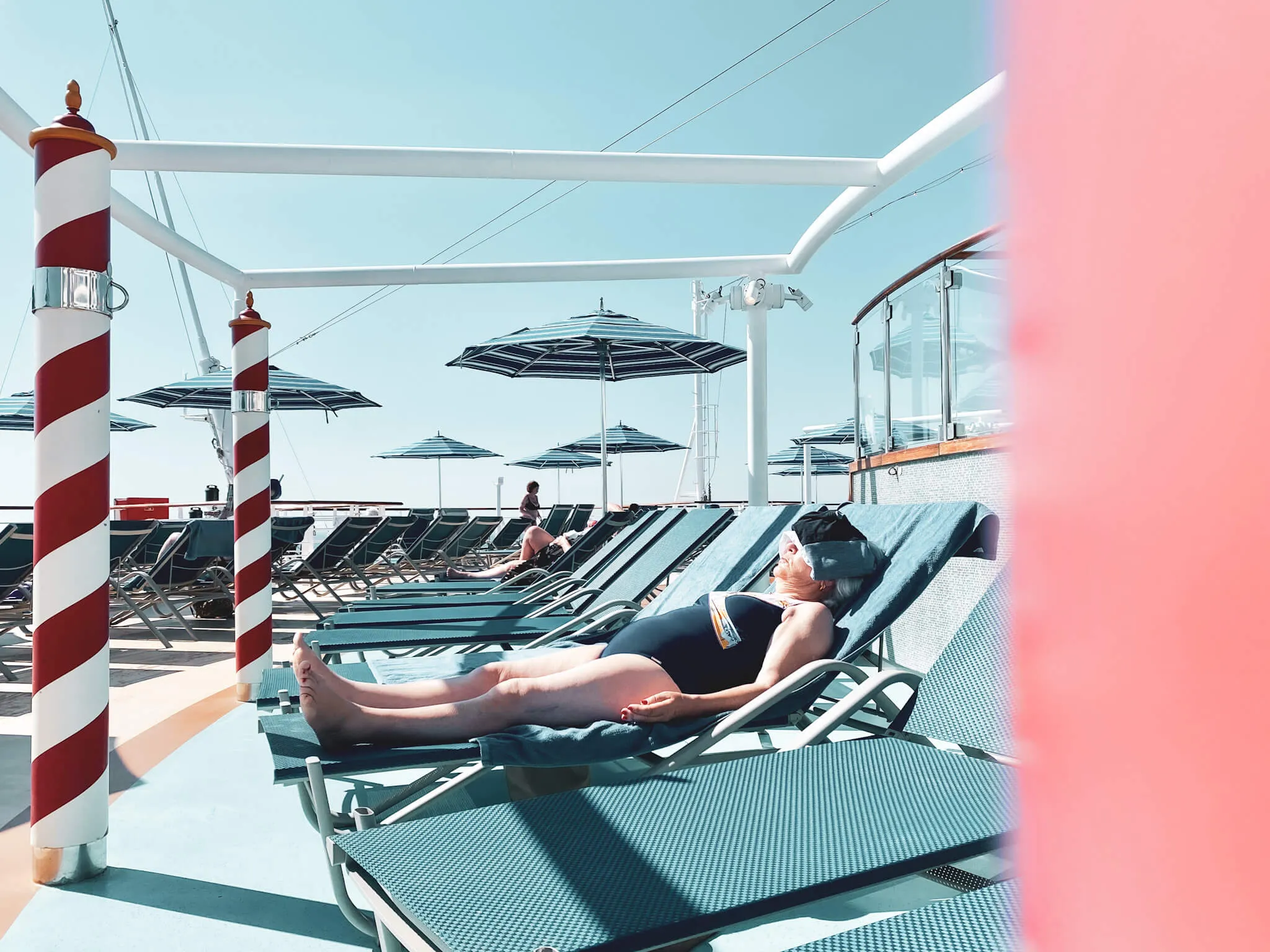 Eine elegante Dame liegt entspannt auf einem Liegestuhl auf dem Deck eines Kreuzfahrtschiffes, mit Sonnenbrille und Buch.