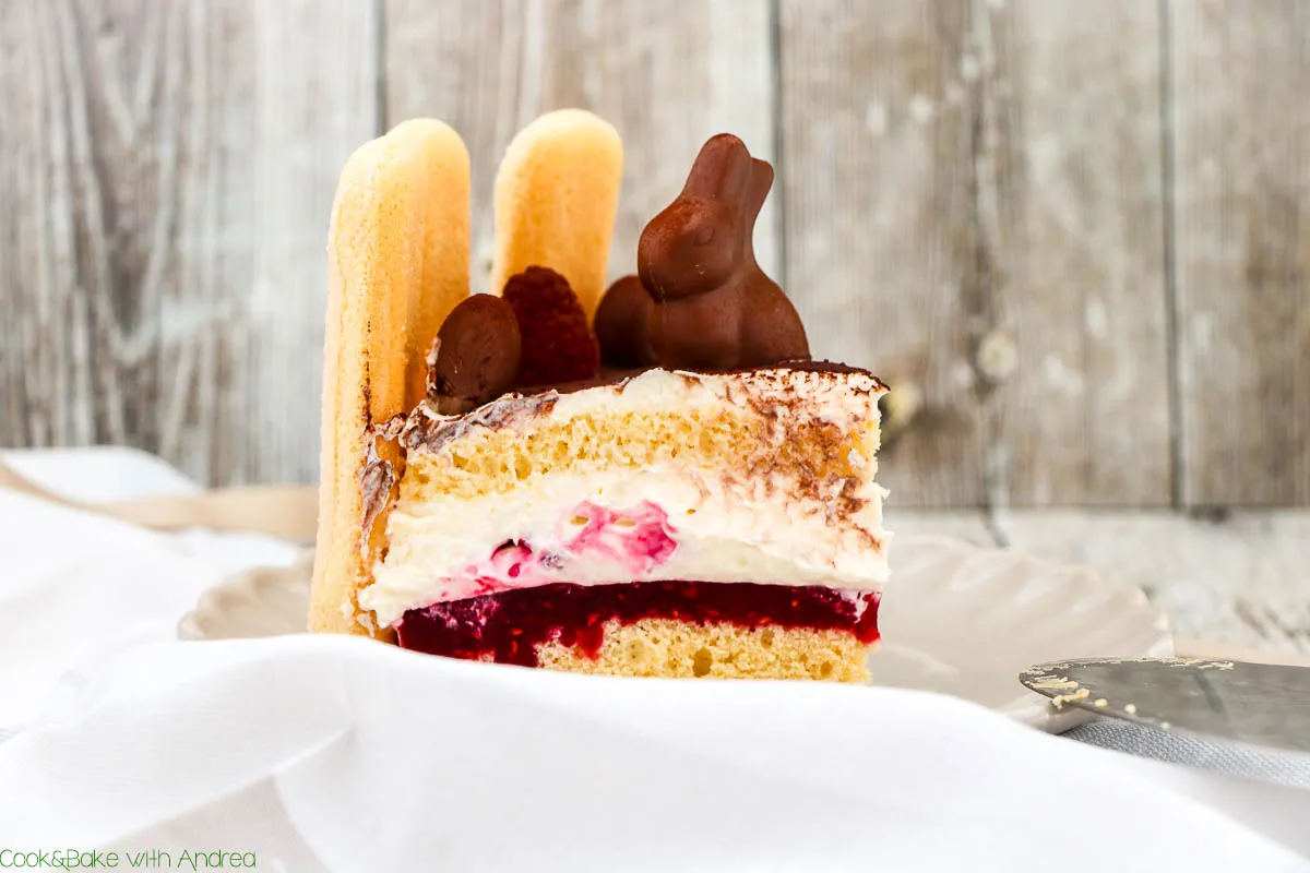 Eine festliche Himbeer-Sahne-Torte auf dem Tisch, bereit für den Osterbrunch, umrahmt von Löffelbiskuit und Schokodeko.