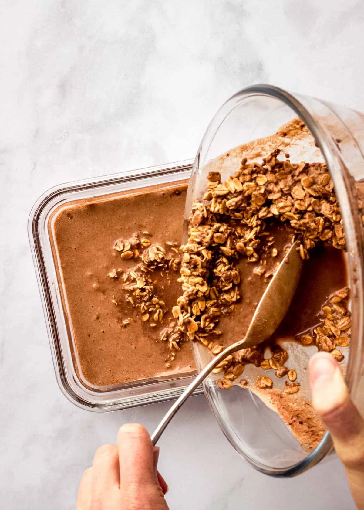 Eine Frau gießt Espresso Overnight Oats aus einer Schüssel in einen luftdichten Aufbewahrungsbehälter.