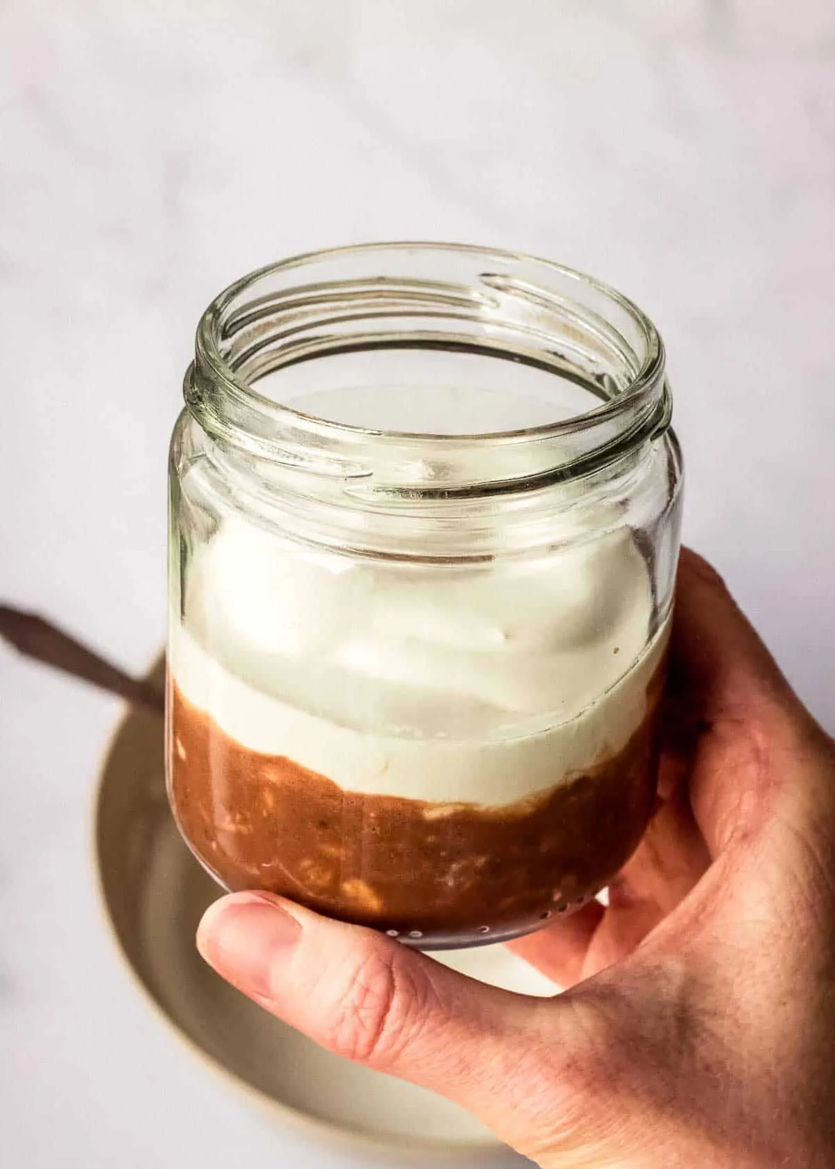 Eine Frau hält ein Glas mit einer Schicht Kaffee Schokoladen Overnight Oats und veganer Mascarpone.